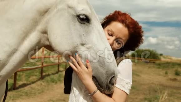 一个红发幸福的女人拥抱一匹白马她的头发在风中飘扬视频的预览图