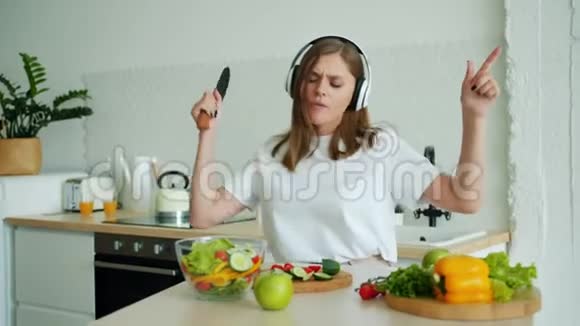 快乐的家庭主妇在家中享用耳机里的音乐厨房视频的预览图