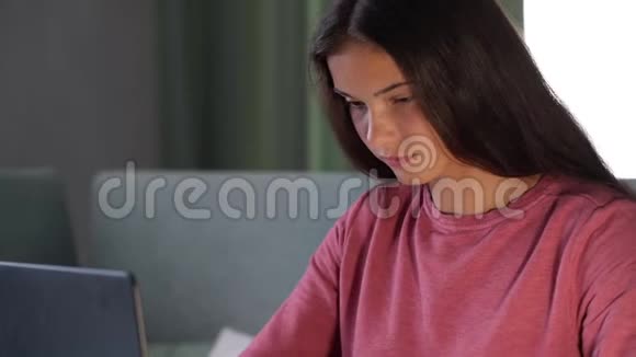 现代笔记本电脑里穿紫色运动衫的布鲁内特学生视频的预览图