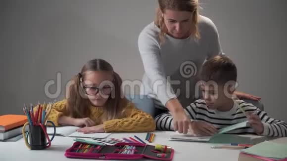 善良的高加索母亲帮助她的孩子做家庭作业戴眼镜的小可爱女孩和她弟弟坐在视频的预览图