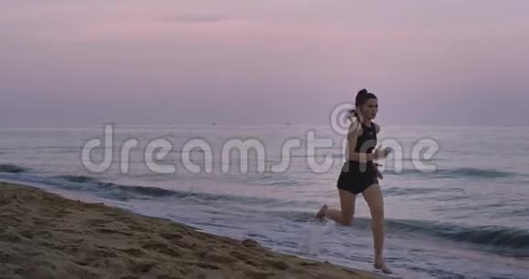 美丽的女士穿着运动服在沙滩上的水中奔跑享受早晨的新鲜空气视频的预览图