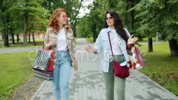 快乐的女人在公园里高达五岁带着购物袋笑着散步视频的预览图