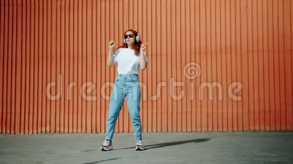 戴着耳机和太阳镜的快乐女孩在街上跳舞玩得开心视频的预览图