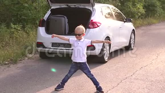 一个快乐的小男孩在有手提箱的汽车后备箱旁边玩得很开心夏季旅行视频的预览图