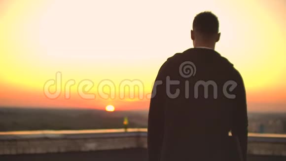 后景日落时分一个穿着连帽衫的男自由职业程序员在屋顶上散步看着美丽的风景喝着啤酒视频的预览图