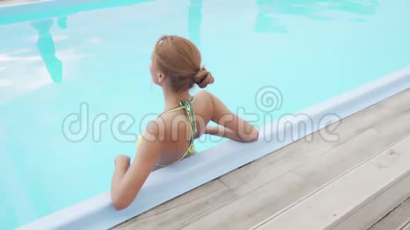 一位身穿比基尼在室外游泳池放松的美女的后景镜头视频的预览图