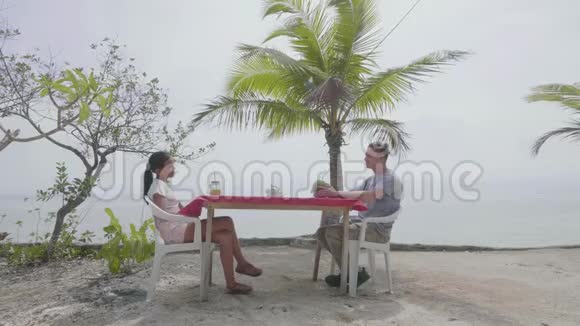 年轻夫妇坐在一个豪华度假胜地海边的一张咖啡桌旁聊天视频的预览图
