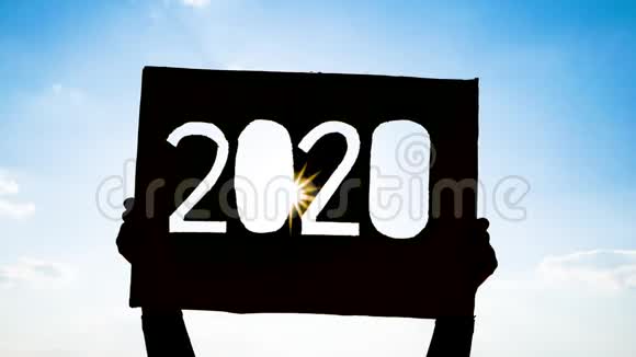 手拿回收纸板的剪影用2020年的文字在蓝天背景和阳光照耀的文字康塞普视频的预览图