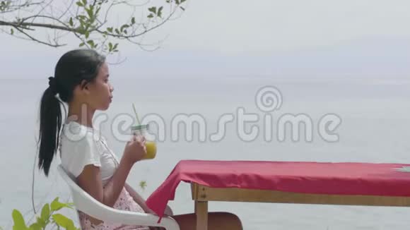 亚洲女孩坐着喝果汁享受宁静的海景视频的预览图