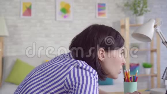 坐在笔记本电脑旁的年轻女子因为弯腰而感到脖子和背部疼痛视频的预览图
