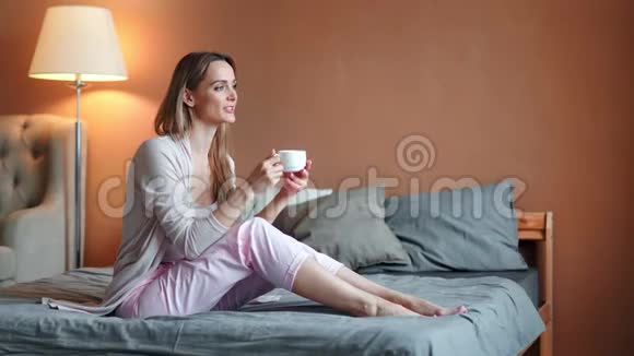 快乐轻松的赤脚年轻女子在卧室喝热茶享受周末在家视频的预览图
