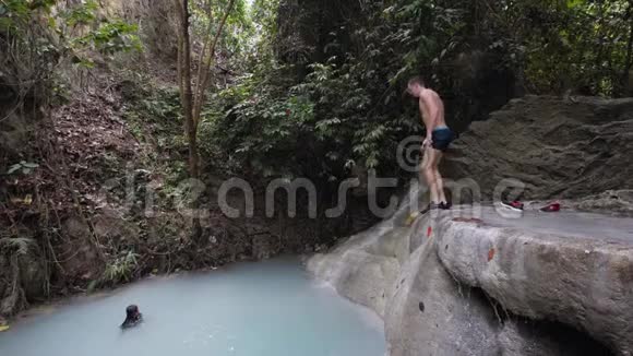 白种人从岩石边缘跳入瀑布的绿松石水中视频的预览图