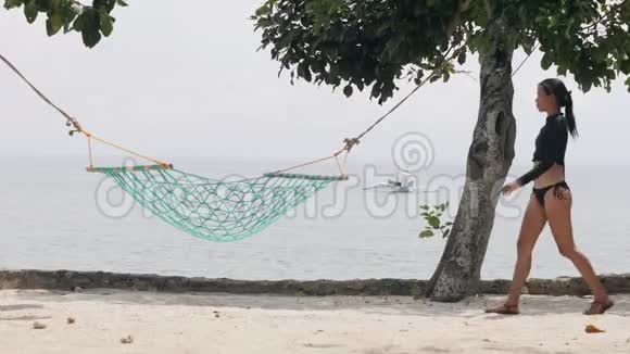 穿着性感泳装的布鲁内特女士躺在海滩上的吊床上视频的预览图