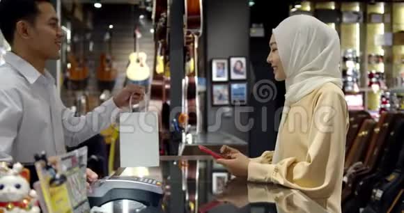 年轻的穆斯林妇女使用智能手机支付非接触式交易机器视频的预览图