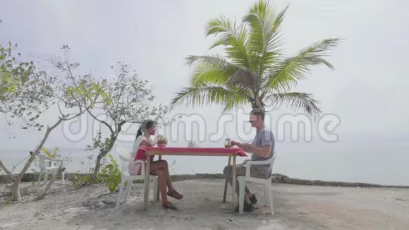 一对年轻夫妇在炎热的夏天在海滩上享受新鲜果汁视频的预览图