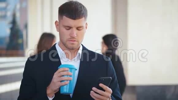 穿着得体的企业家站在他的办公室旁喝咖啡去吧在他的智能手机上输入信息人民视频的预览图