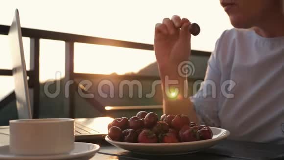 一个女人在日落时吃成熟的Krasnfe浆果草莓和樱桃放在火炬里放在桌子上放在阳光下视频的预览图