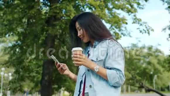 亚洲学生在公园散步用智能手机喝酒微笑着去喝咖啡视频的预览图
