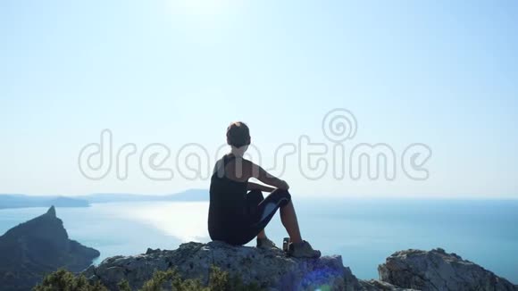 一个快乐的徒步旅行者女人坐在山顶上放松从高处欣赏美妙的景色青年视频的预览图