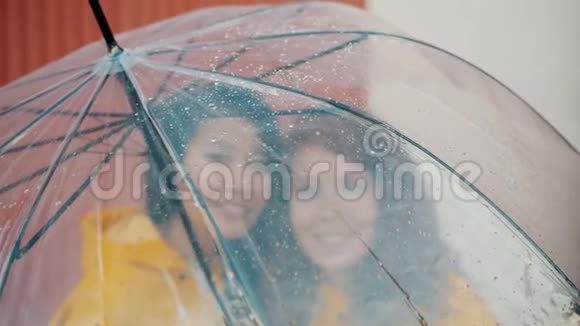 穿着雨衣伞下的漂亮女孩站在一起微笑视频的预览图