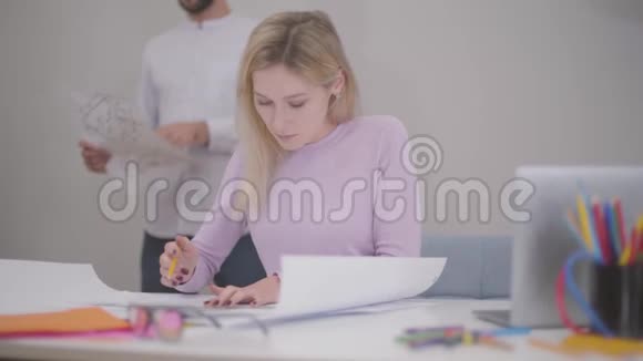 美丽的金发白种人妇女在办公室绘制蓝图的肖像她的男同事站在视频的预览图
