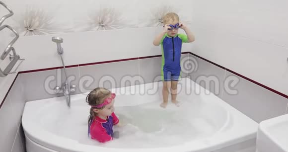 穿着蓝色游泳眼镜的小男孩正在跳着游泳衣一个穿着泳衣的女孩在抓和帮助她的哥哥视频的预览图