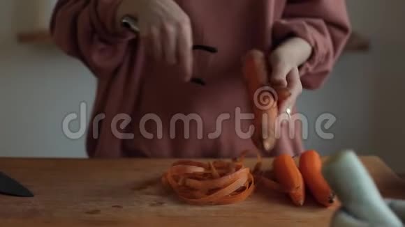 一个女孩用一把特殊的刀子在厨房的台面上用一把平底锅剥了一根胡萝卜的手视频的预览图
