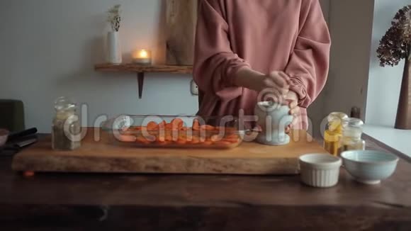 厨房餐桌上的那个女孩在一个玻璃碗切好的胡萝卜旁边的灰浆里除香料特写视频的预览图