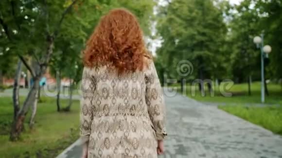 一个人在公园散步的红发女孩的后景转向镜头微笑视频的预览图