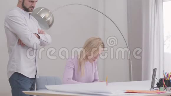 侧面看年轻的高加索女性建筑师在办公室绘制蓝图她的男同事控制着视频的预览图