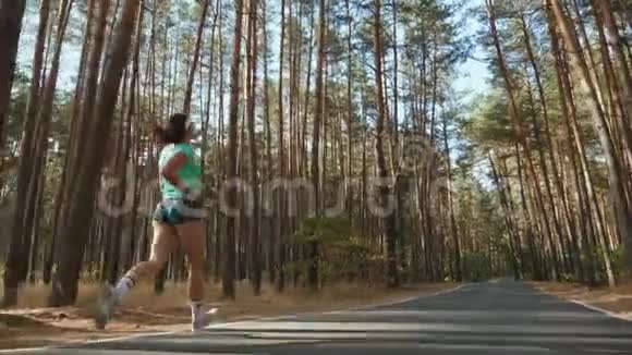 运动女孩在松林中沿着道路奔跑视频的预览图