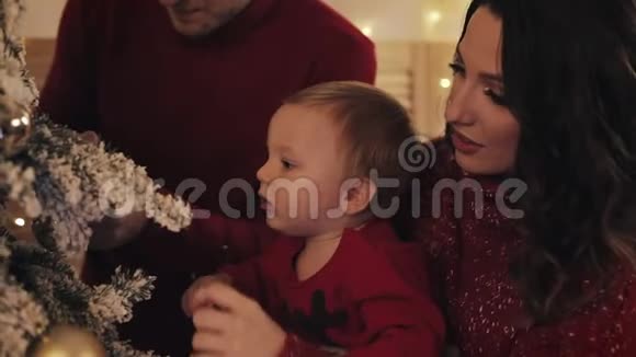 幸福的微笑家庭与小宝宝站在圣诞树和装饰树附近舒适的客厅放大妈妈视频的预览图