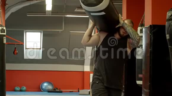 一个男健美运动员肩上扛着拳击袋把它放下视频的预览图