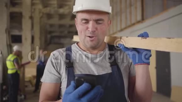戴着白色头盔的成年白种人建筑工人的肖像像看智能手机一样大声笑出来强壮的肌肉男视频的预览图