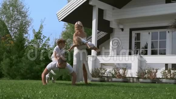 年轻的一家人爸爸和两个儿子在房子附近的草地上做早操视频的预览图