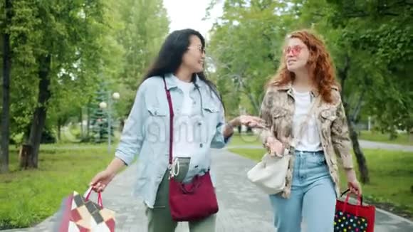 快乐的女孩朋友们拿着购物袋在公园散步笑着说视频的预览图