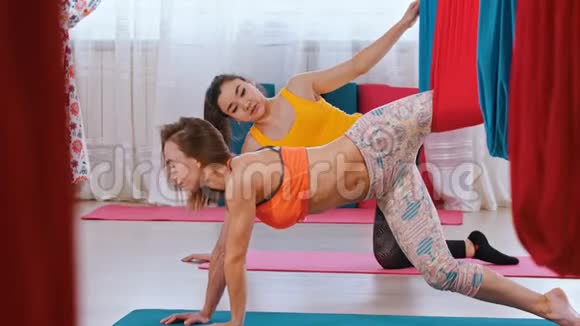 空中瑜伽一个女人和她的教练做运动靠在垫子上的手他们的一条腿挂在上面视频的预览图