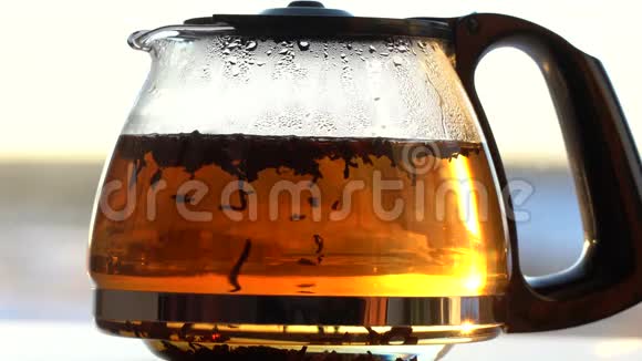 一个茶壶茶是用透明的玻璃在朝阳的照射下制成的在玻璃茶壶里漂浮的红茶颗粒视频的预览图