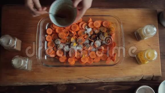 一个年轻的女孩正在一个大玻璃碗里用香料在切碎的胡萝卜上倒入酱汁从上面看特写视频的预览图