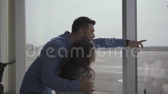 从侧面可以看到年轻留胡子的白人男子通过机场窗口展示飞机小美女等着视频的预览图