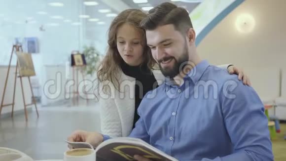 漂亮的白人女孩棕色卷发在杂志上展示照片和她父亲聊天有钱人在等视频的预览图