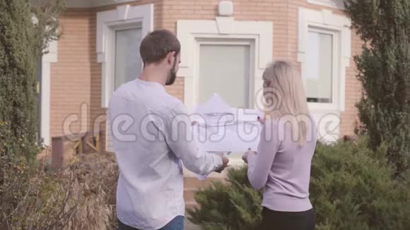 男性白种人建筑师和他的女性助理在房子前面检查蓝图并给予高五视频的预览图