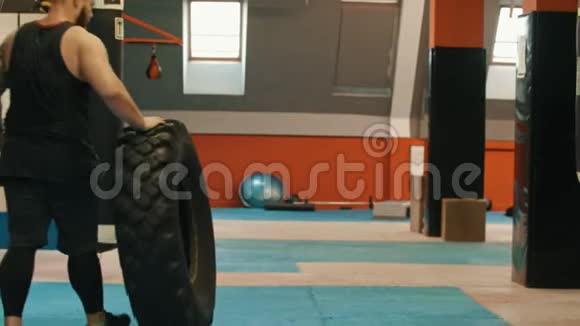 一个男子健美运动员在体育馆里滚动一个大轮胎视频的预览图