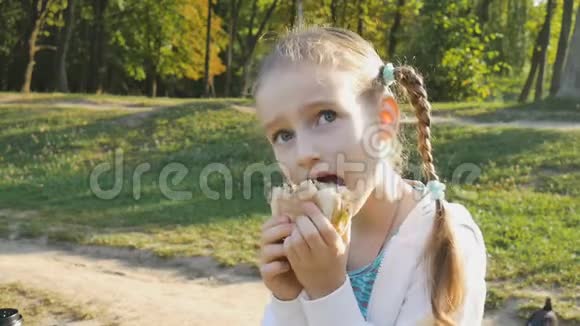 小金发女孩正坐在公园的长凳上吃汉堡包儿童营养不良生活方式不健康视频的预览图