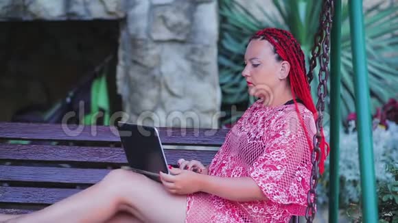 年轻的女性自由职业者正在家里院子里的秋千上用笔记本电脑工作视频的预览图