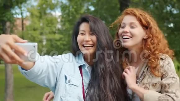 可爱的女孩在绿色公园里用智能手机摆姿势自拍拥抱微笑视频的预览图