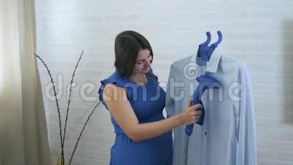 一个年轻的孕妇摸了摸她的胃用蒸汽抚摸男人衬衫蒸衣服的过程视频的预览图
