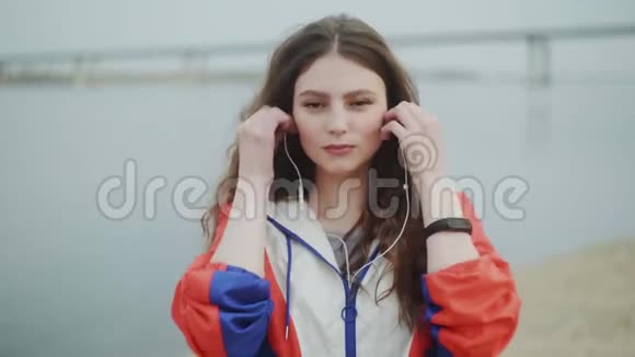 年轻女子在镜头前晃晃悠悠戴着耳机听音乐进行有氧训练背景是河流视频的预览图