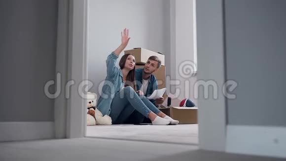 喜笑颜开的一对恋爱中的情侣坐在新公寓的地板上讨论的设计视频的预览图