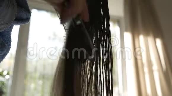 布鲁内特女孩吹干湿发背景下的太阳光线靠近窗户女人正在给头发做造型视频的预览图